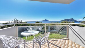 Ein Balkon mit Glastisch und Stühlen, mit Blick auf ein Gewässer und ein entferntes Gebirge.