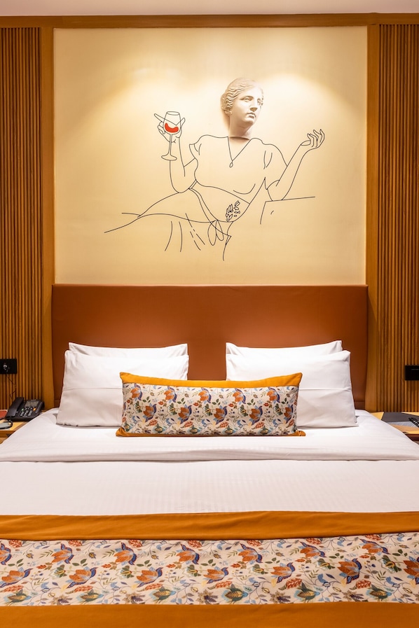 A neatly made bed with white linens and a floral-patterned pillow, a wall-mounted artwork depicting a figure holding a glass, and wooden paneling on the walls.
