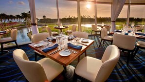 Un espace repas avec des tables préparées pour deux personnes, offrant une vue sur un terrain de golf et un plan d’eau.