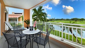 Un balcon avec une table et des chaises, donnant sur un terrain de golf et un plan d’eau.