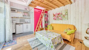 A compact room with a kitchenette, a sofa, a table with a tablecloth, and a ladder. - Pretty Little Chalet on the Silver Coast (Le Porge)