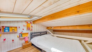 A compact room with a bunk bed, wooden walls, a small shelf with books, and a string of red and yellow decorations. - Pretty Little Chalet on the Silver Coast (Le Porge)