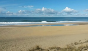 Una playa con una extensa zona arenosa, un mar tranquilo y un cielo despejado.