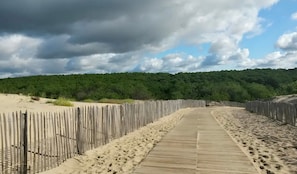 A wooden boardwalk leading through a sandy area with a forested hill in the background. - Guest Room "La Côte d’Argent Océane" with Private Terrace, Private Garden, and Wi-Fi (Le Porge)