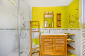Un baño con ducha, tocador de madera, espejo y pared de acento amarilla.