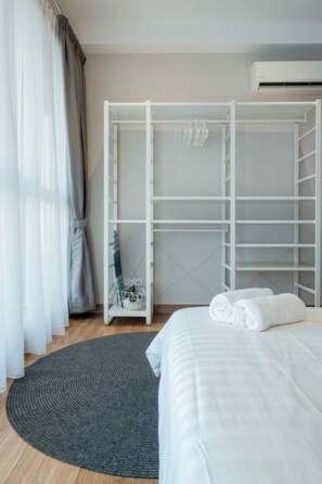 Une chambre à coucher avec un lit, un tapis gris, une armoire blanche et une fenêtre avec des rideaux gris.