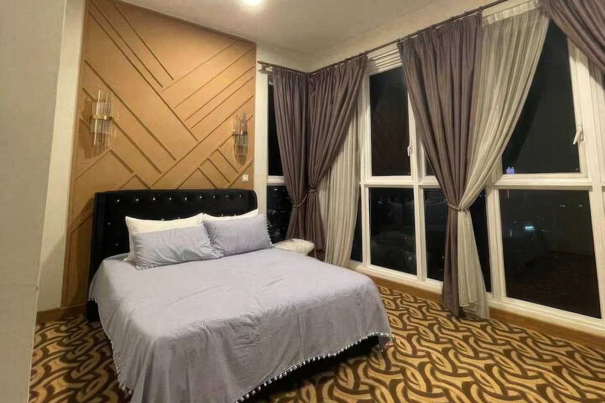 Une chambre d’hôtel avec un lit, une moquette à motifs, un mur décoratif en bois et une fenêtre avec des rideaux.