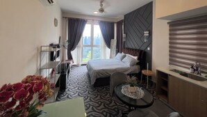 Een hotelkamer met een bed, een bureau, een stoel, een klein tafeltje met een plant en een raam met gordijnen.