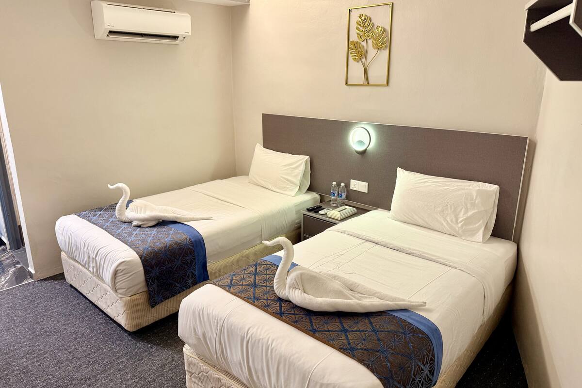 Een hotelkamer met twee bedden, een nachtkastje, een wandairconditioner, een wandlamp en een decoratieve plant.