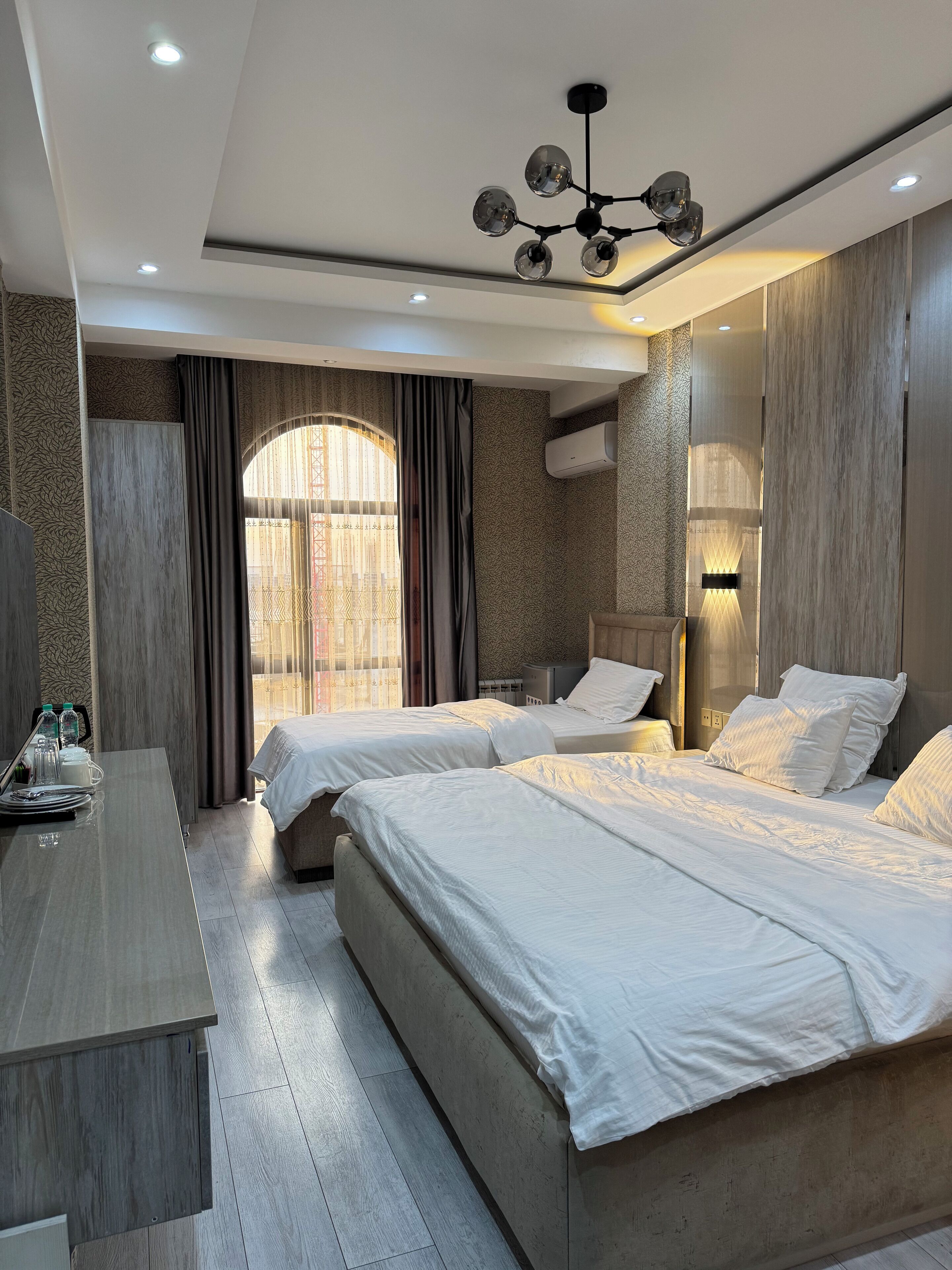 Une chambre d’hôtel avec deux lits, un bureau et une grande fenêtre avec des rideaux.