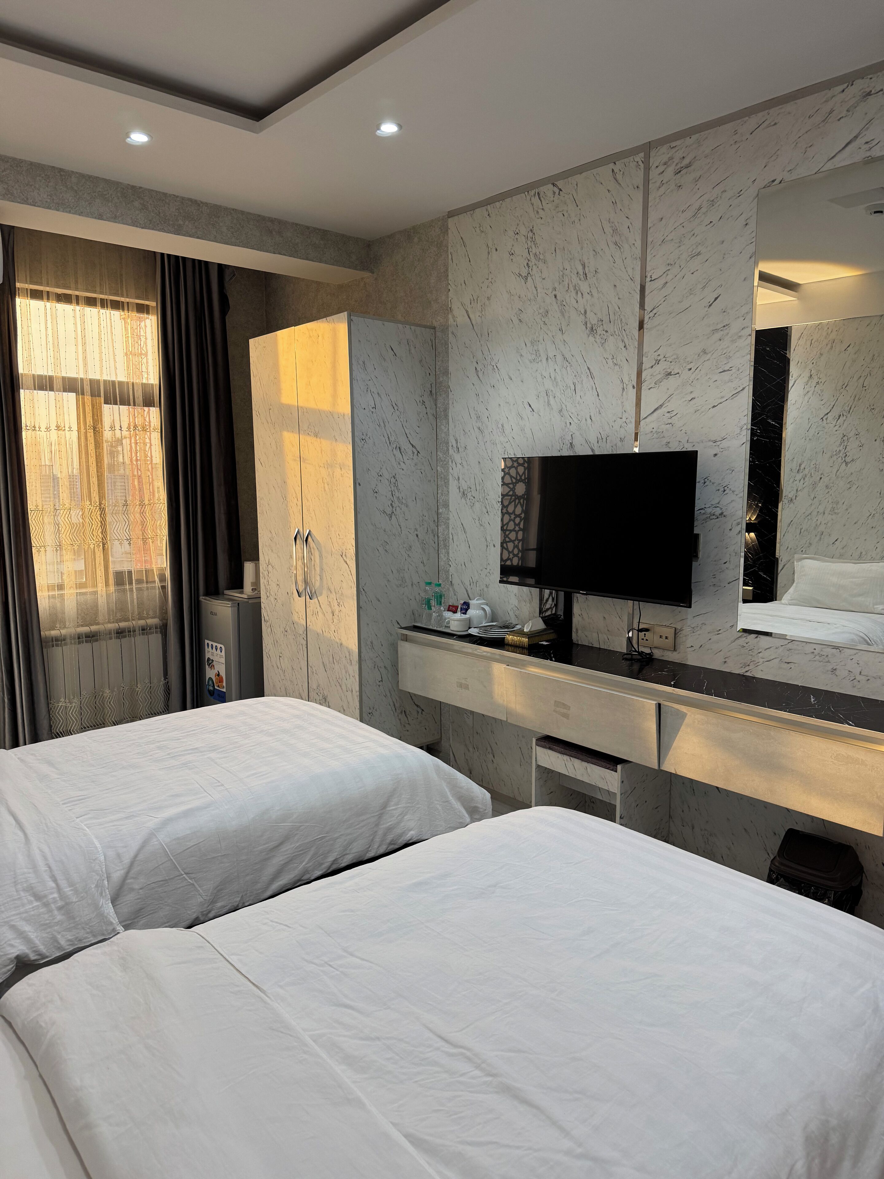 Une chambre d’hôtel avec deux lits, un bureau doté d’un téléviseur à écran plat, un minibar et une grande fenêtre avec des rideaux.
