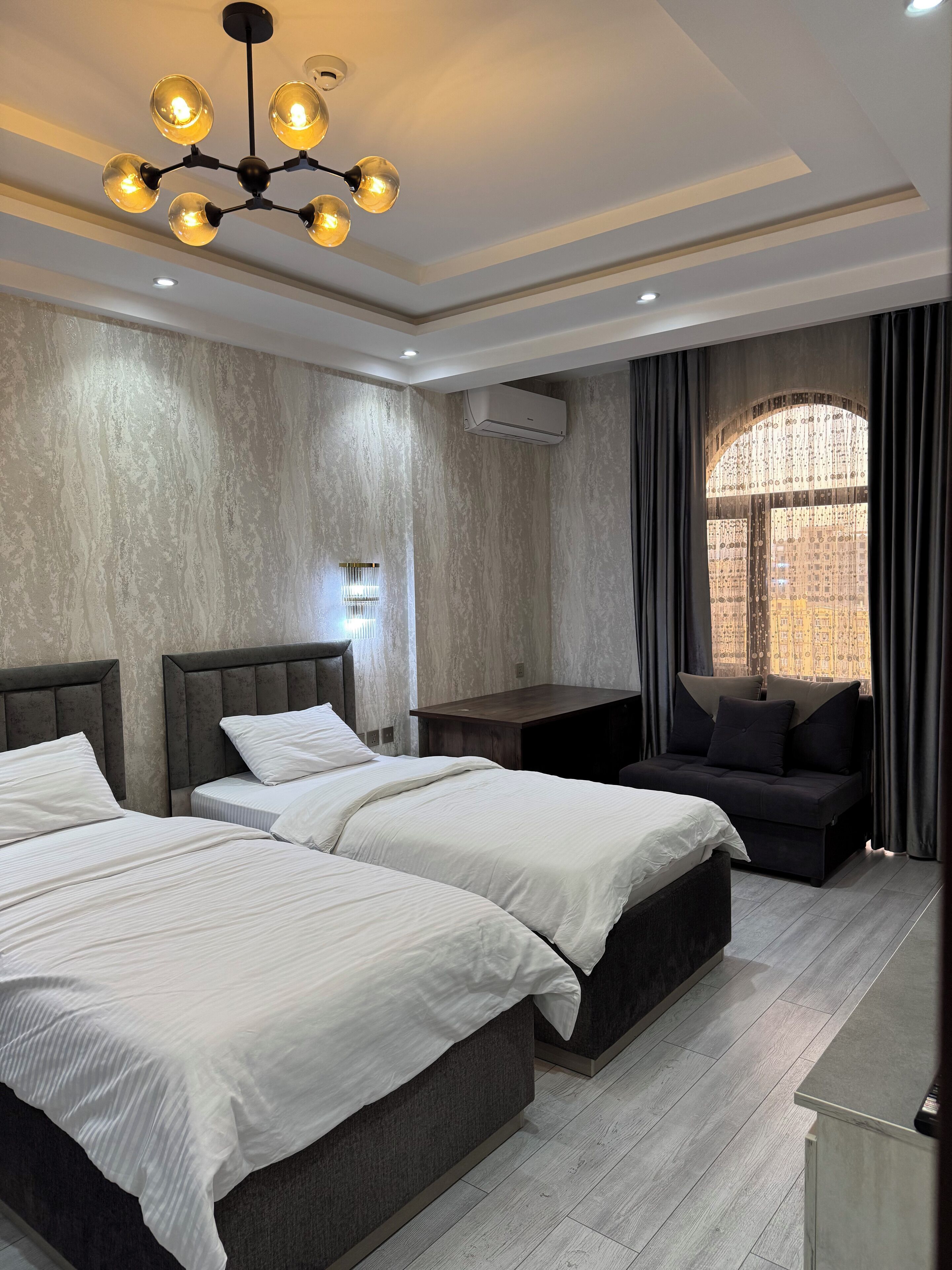 A hotel room with two beds, a desk, and a large window with curtains.