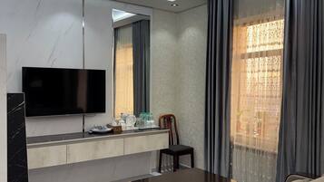 A modern living room with a flat-screen TV, a dining table, a sofa, and a chandelier.