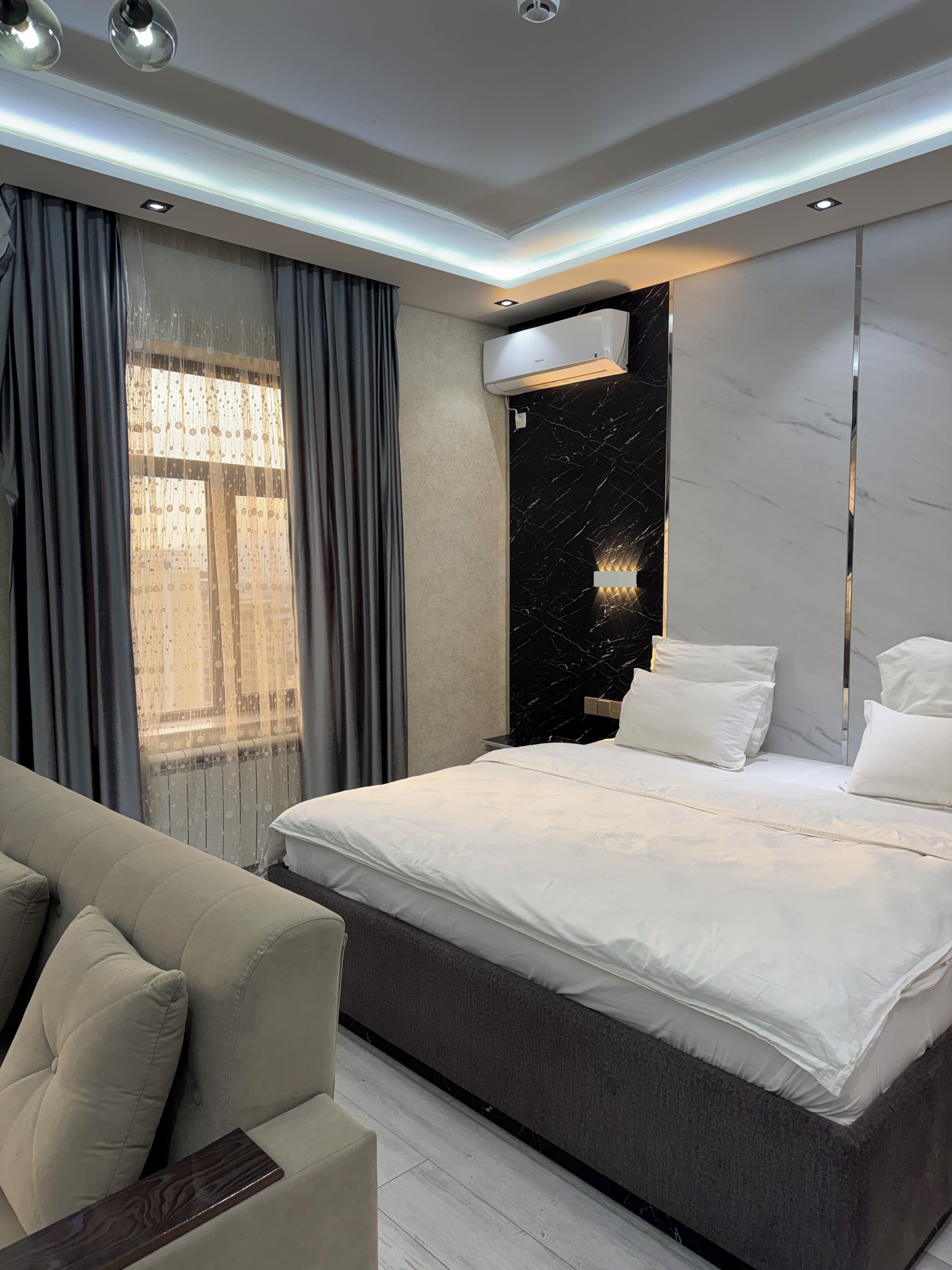 A modern bedroom with a large bed, a sofa, and a marble accent wall.