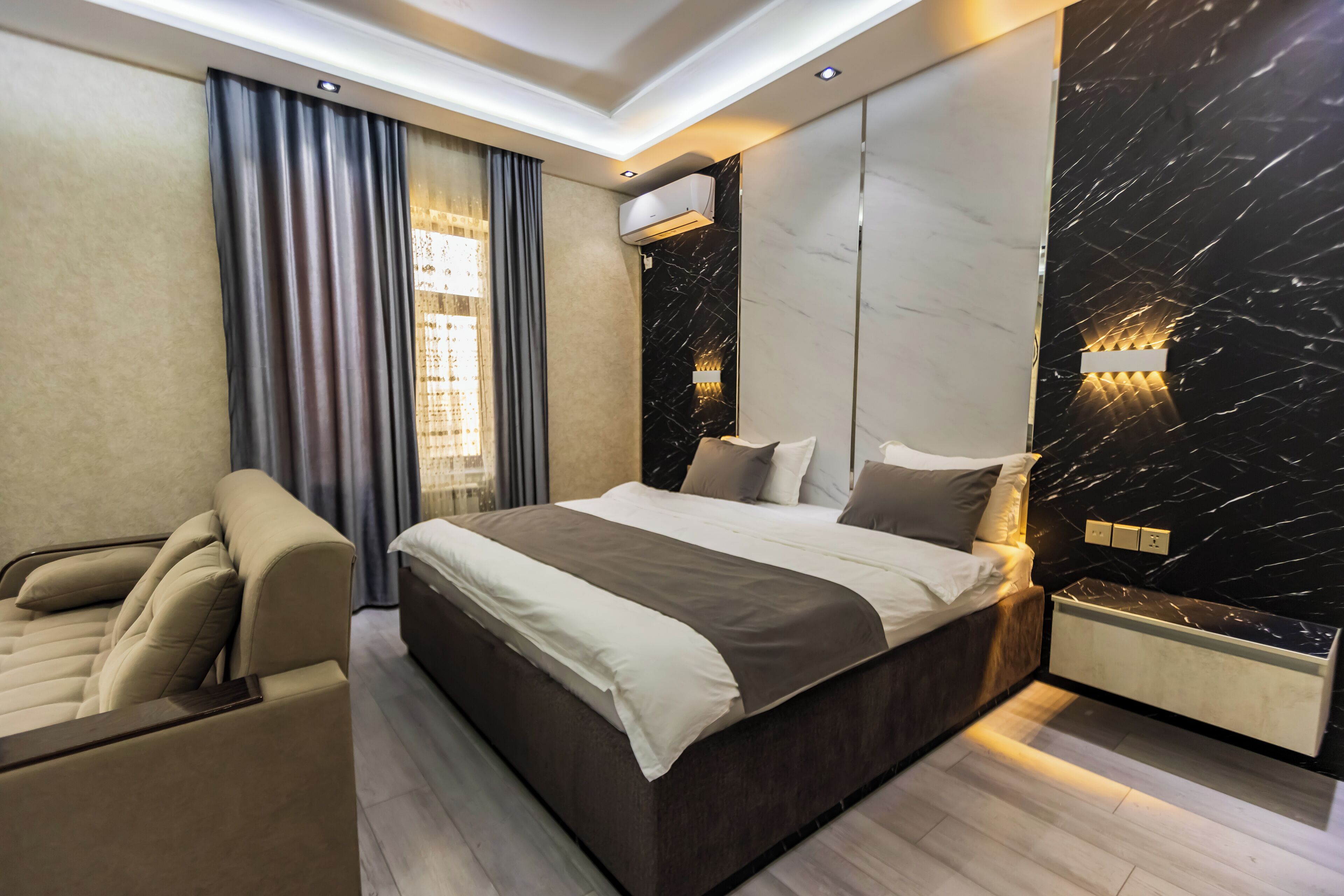 Quarto moderno com uma cama grande, um sofá, ar condicionado fixado na parede e parede com padrão marmorizado.