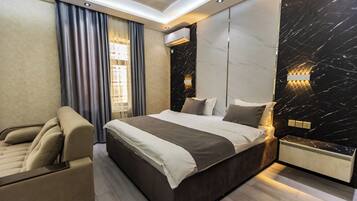 Quarto moderno com uma cama grande, um sofá, ar condicionado fixado na parede e parede com padrão marmorizado.