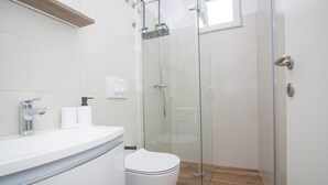 Um banheiro moderno com box de vidro, vaso sanitário branco e toucador com espelho e duas torneiras.