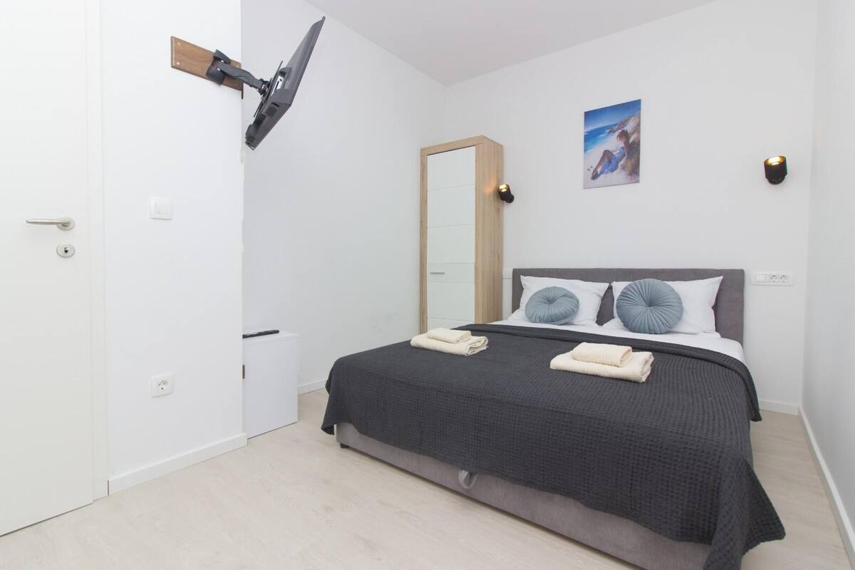 A modern bedroom with a bed, a wooden door, a wall-mounted TV, and a painting.