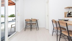 Uma área de refeições compacta com uma mesa de madeira e quatro cadeiras, uma pequena planta em vaso e uma estante com objetos.