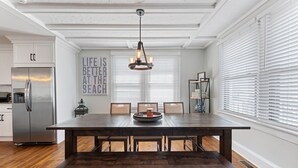 Un vaste espace dédié à la salle à manger, avec une table et des chaises en bois, un lustre et une cuisine en arrière-plan.