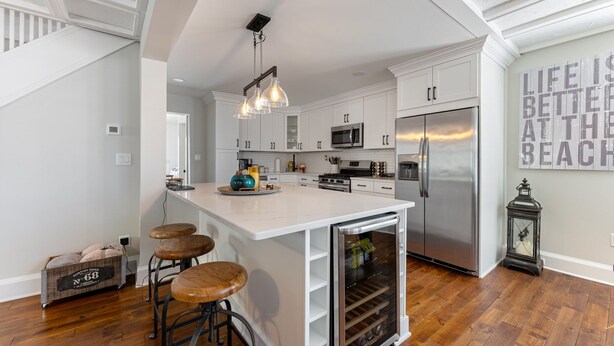 Une cuisine moderne avec des meubles blancs, un grand îlot central doté de tabourets, des appareils en acier inoxydable et une lanterne décorative.