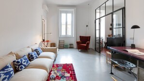 A modern living room with a sofa, a red armchair, a desk, and a large window. - Splendid two-room apartment Dateo - Mirable PM (Milano)