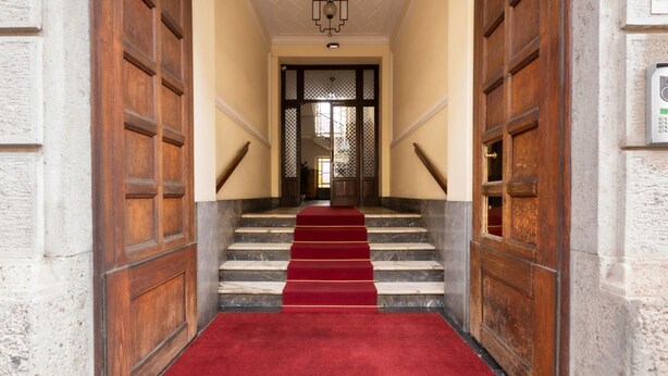 A grand staircase with a red carpet leading to a wooden door at the top. - Splendid two-room apartment Dateo - Mirable PM (Milano)