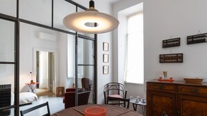 A modern dining area with a round table, chairs, a hanging light fixture, and a wooden cabinet with decorative items. - Splendid two-room apartment Dateo - Mirable PM (Milano)