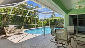 A covered outdoor area with a pool, seating, and a view of greenery.