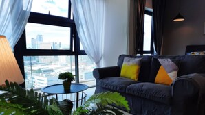 Un salon moderne doté d’une grande fenêtre, d’un canapé en cuir noir agrémenté de coussins colorés, d’une petite table ronde sur laquelle est posée une plante en pot et d’une lampe.