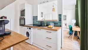 A modern kitchen with white cabinetry, a wooden countertop, a built-in washing machine, and a dining area with a table and chairs.