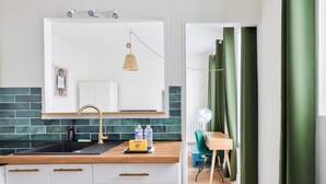 A modern kitchen with a white countertop, a gold faucet, and a green backsplash. There is a welcome sign on the counter, and a fan is visible in the background.