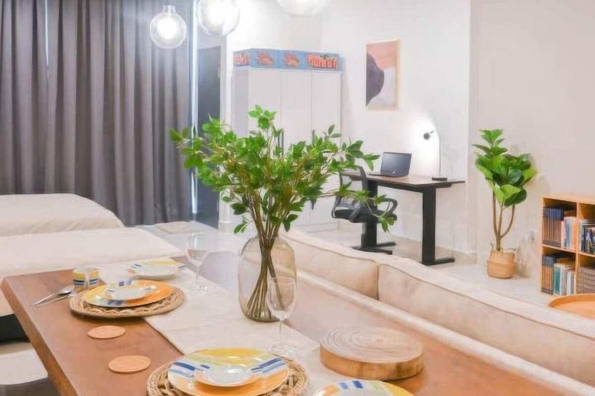 Une chambre d’hôtel moderne avec une table à manger dressée pour deux personnes, un ordinateur portable sur un bureau et une bibliothèque.