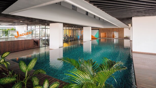 A modern indoor swimming pool with clear water, surrounded by wooden decking and tropical plants. - Luxstay Atria Sofo Suites Apartments (Petaling Jaya)