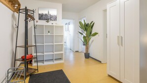 A hallway with a wooden staircase, a metal coat rack, white shelving units, a potted plant, and a white wardrobe. - Big groups / Families / Exhibition (Duisburg)