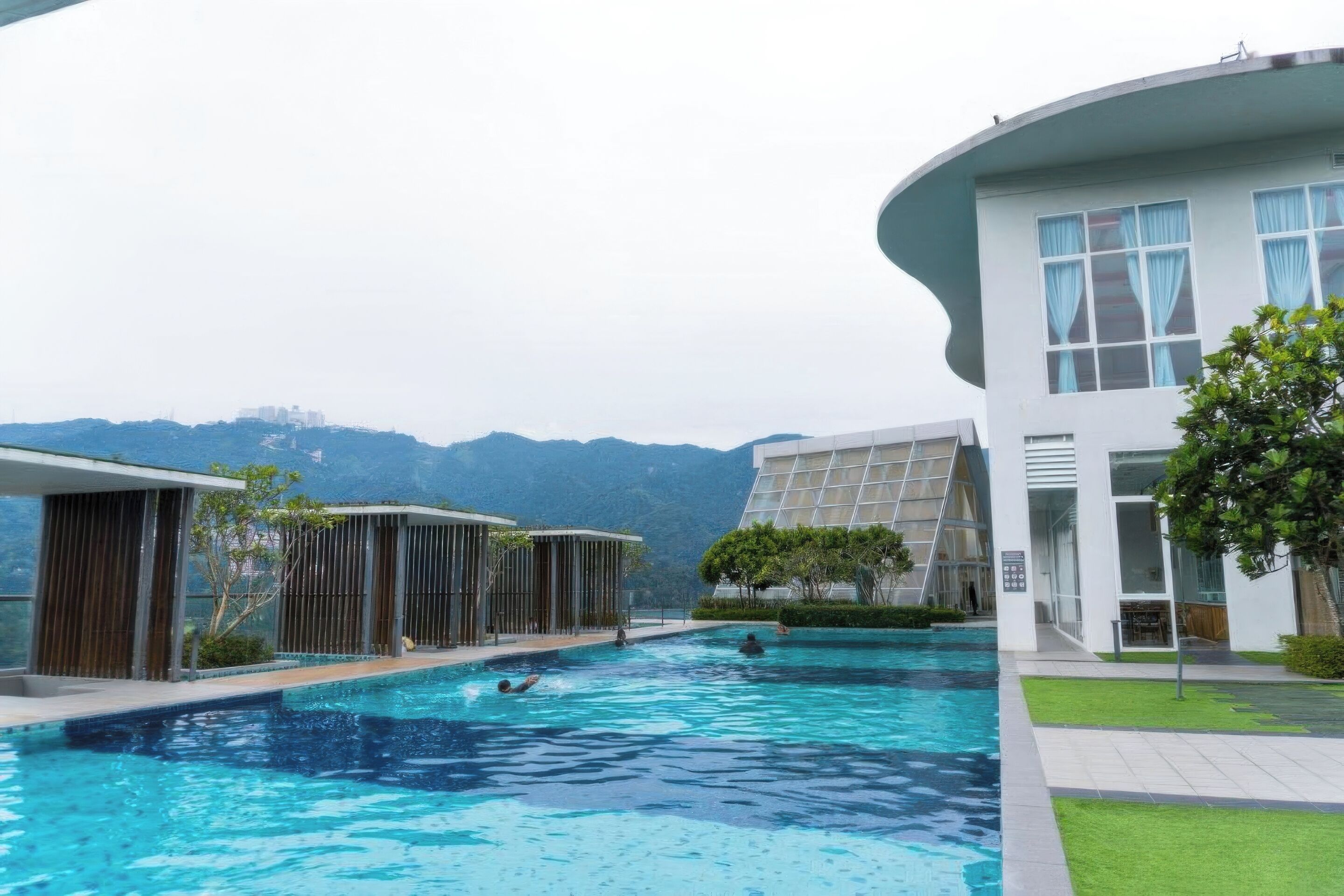 A swimming pool area with modern architecture, a view of mountains, and a well-maintained lawn.