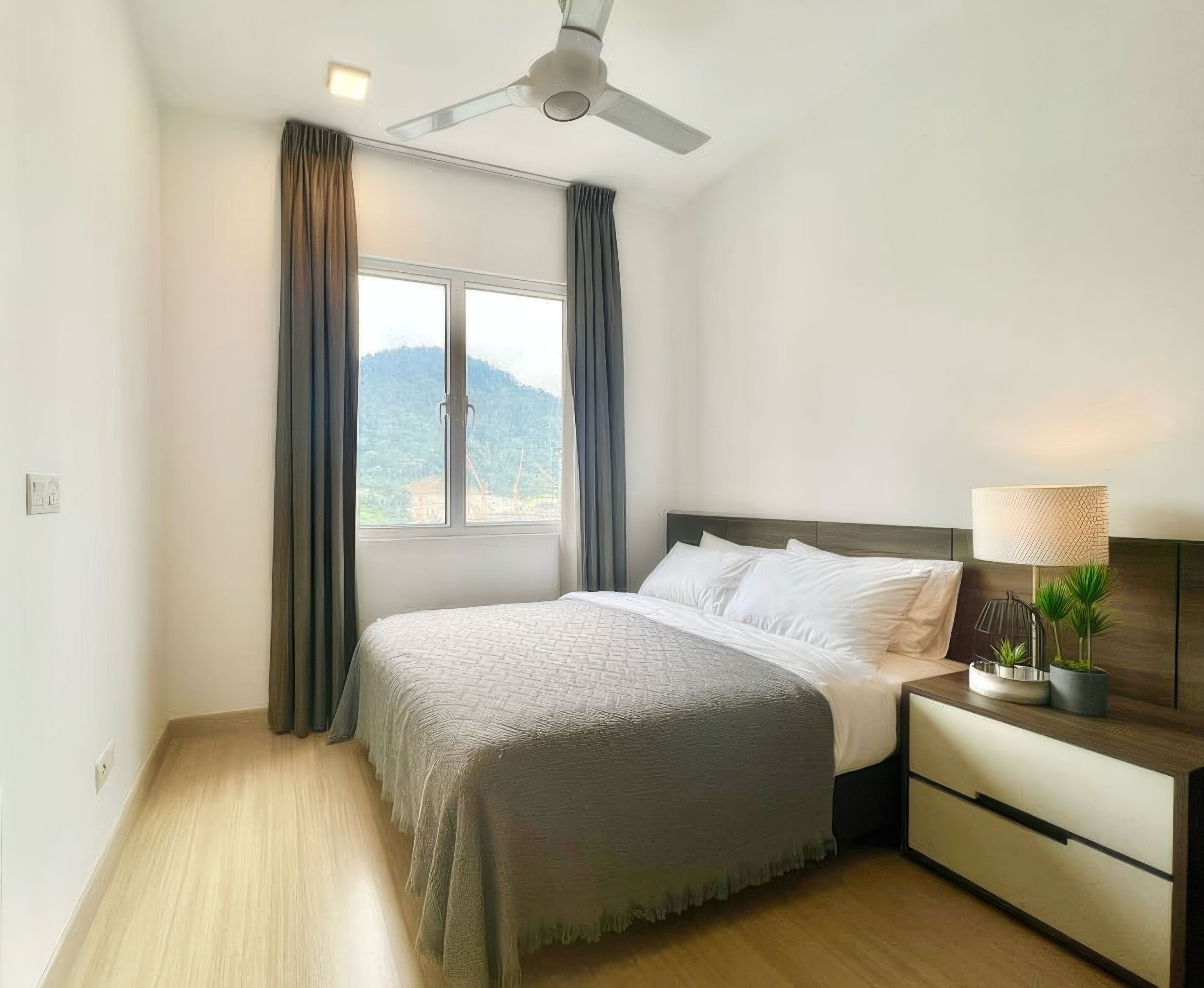 A bedroom with a bed, a nightstand, a lamp, and a view of a mountain through a window.