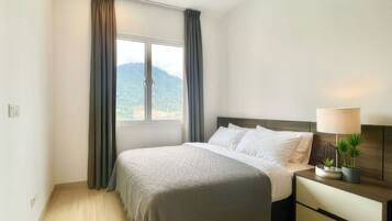 A bedroom with a bed, a nightstand, a lamp, and a view of a mountain through a window.