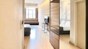 A modern hotel room with a large bed, a seating area with a sofa and a small table, a TV, and a large mirror.