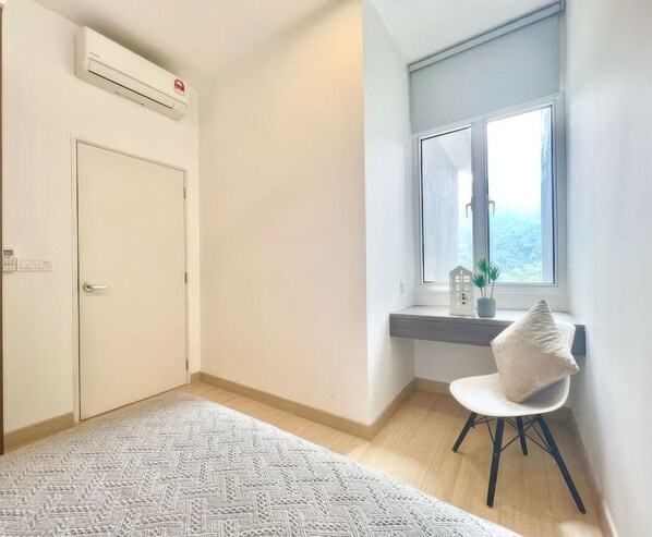Una habitación con una puerta blanca, una ventana con vistas, una mesita con una planta, una silla blanca y una alfombra estampada.