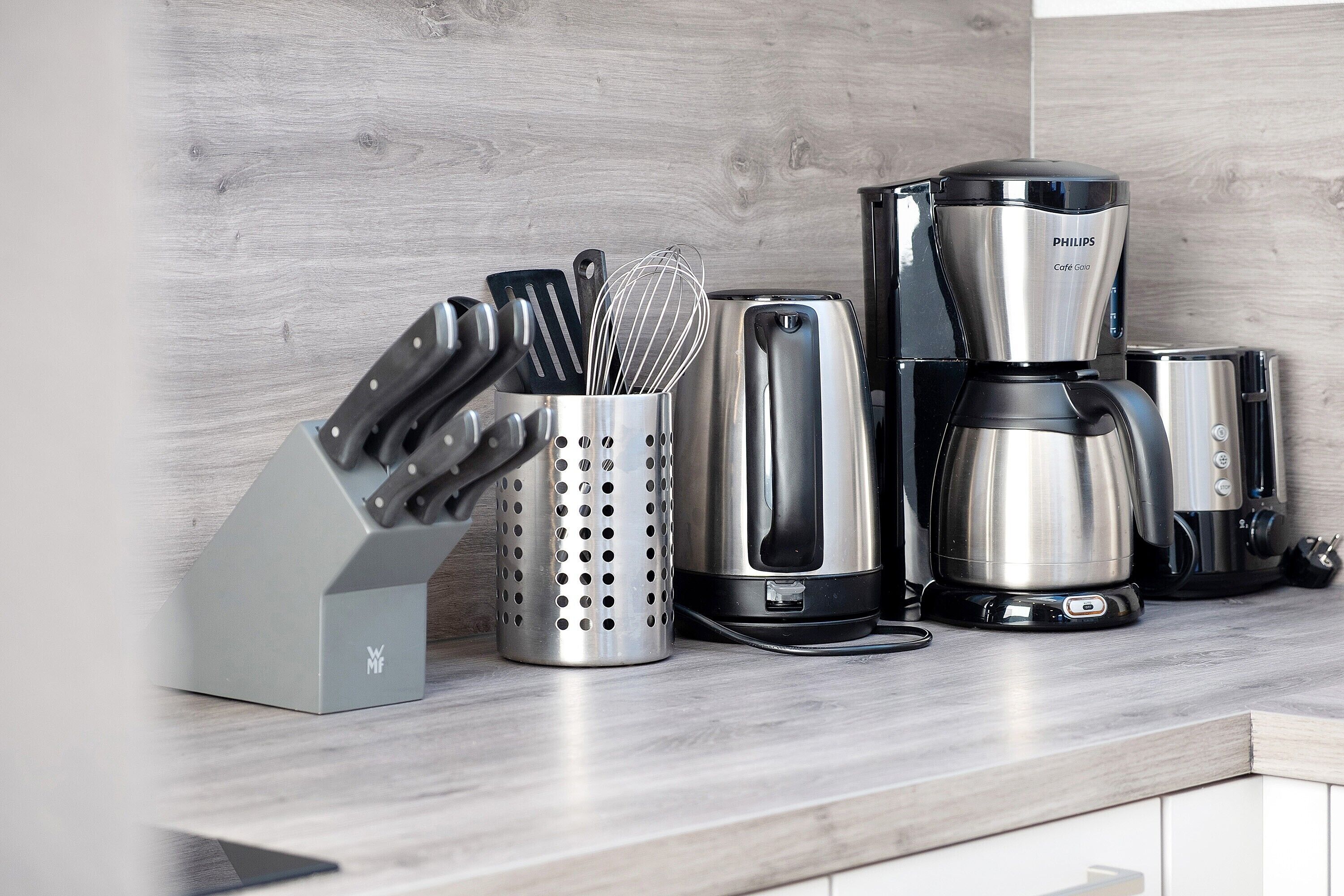 A kitchen counter with a coffee maker, a knife block, and a whisk holder.