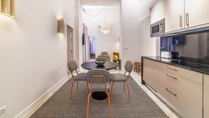 A narrow kitchen with a dining area, featuring a round table with checkered chairs, a microwave, and a modern stove.