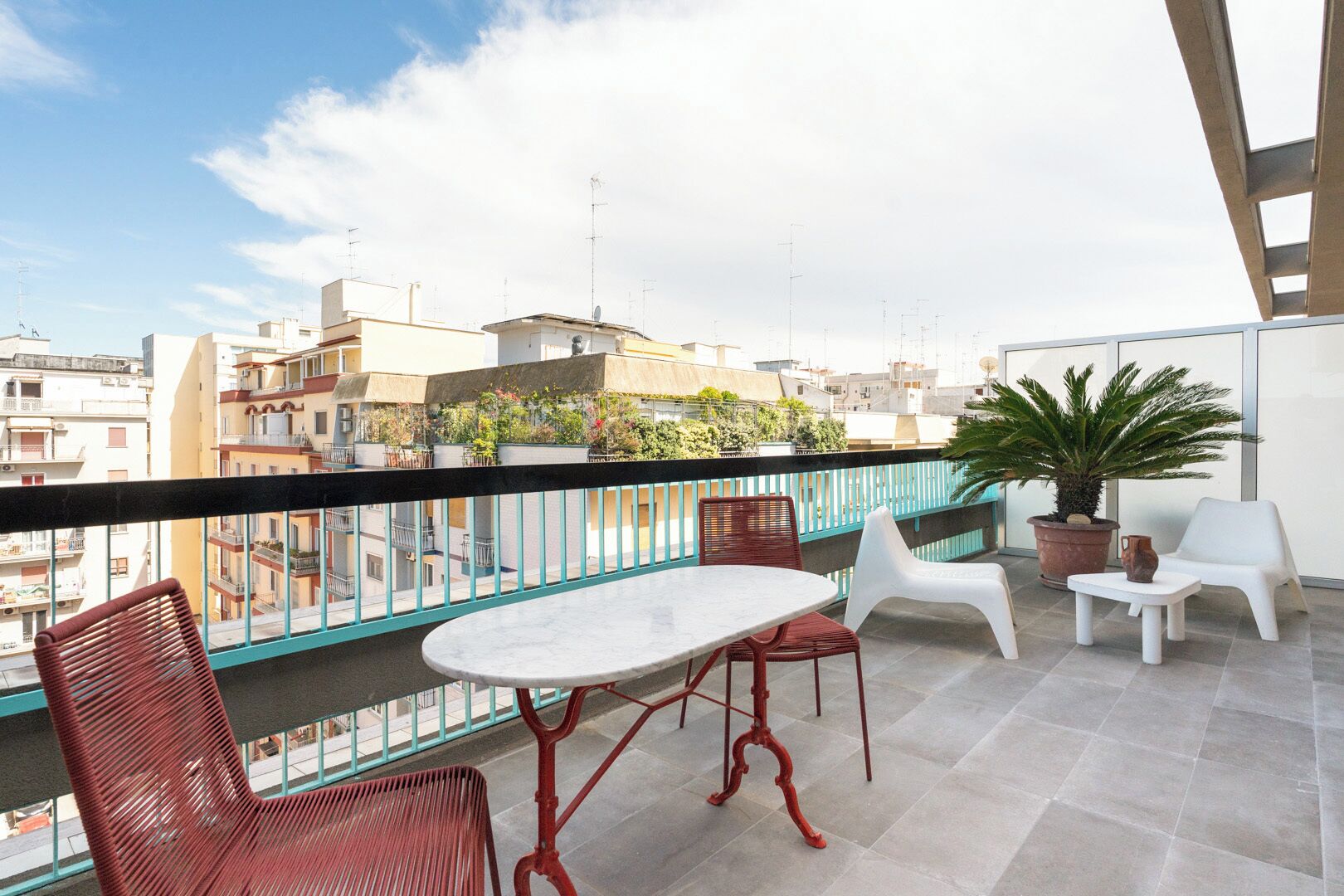 A balcony with a table and chairs, potted plants, and a view of surrounding buildings.