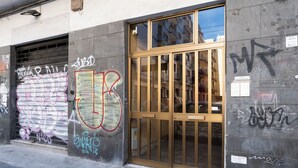 Un bâtiment doté d’une porte à volet métallique fermée, d’une grande fenêtre avec un cadre en bois et de divers graffitis sur les murs.