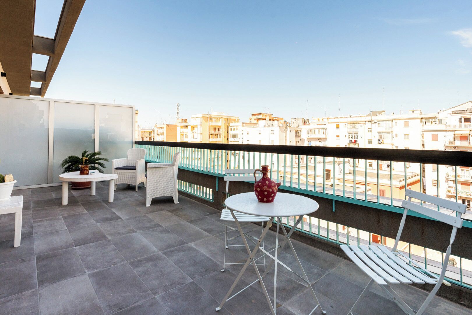 A balcony with a table and chairs, a potted plant, and a decorative vase.