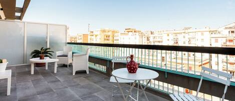 A balcony with a table and chairs, a potted plant, and a decorative vase.