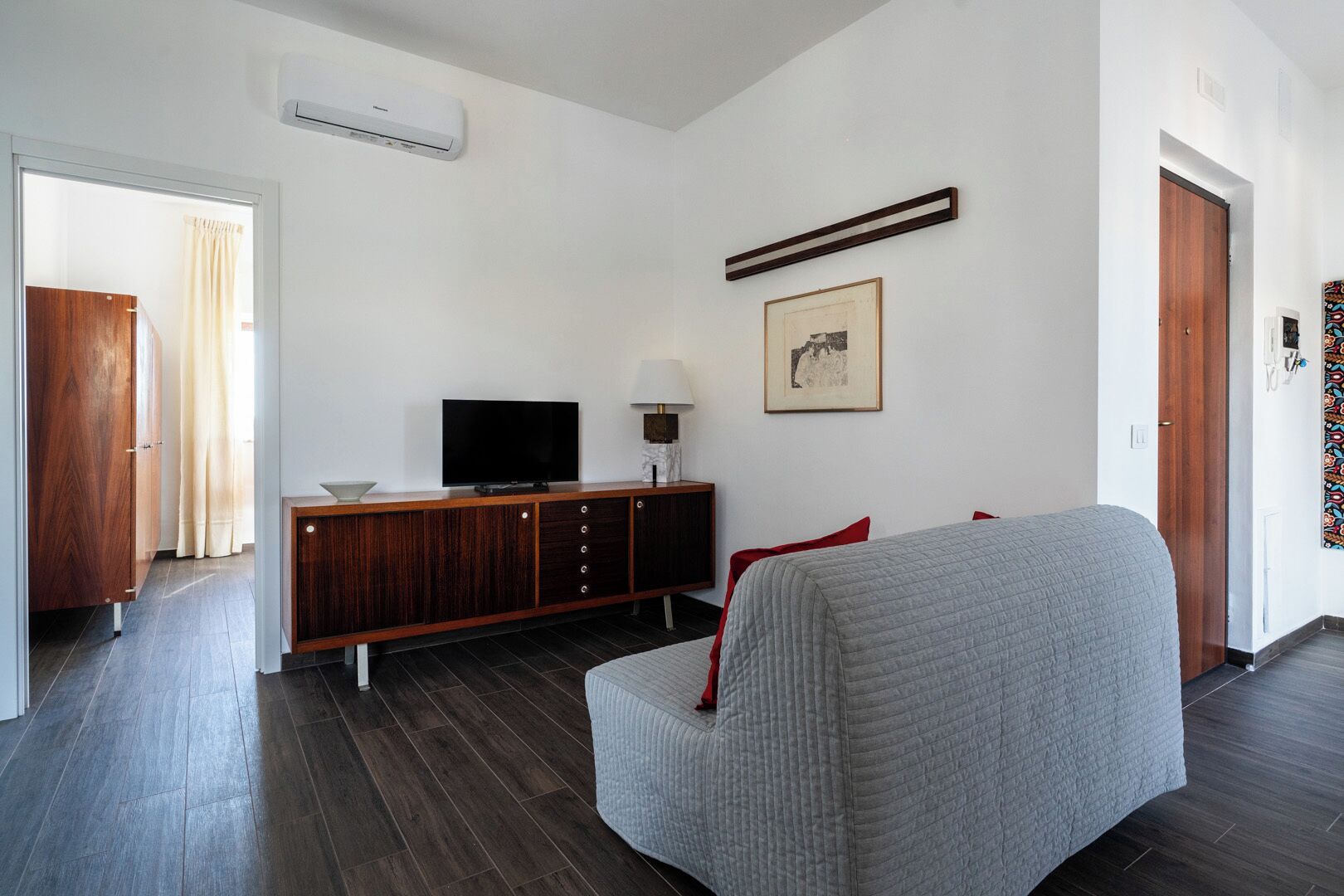 Uma sala de estar moderna com um sofá cinza, um armário de madeira com uma televisão de tela plana e um quadro pendurado na parede.
