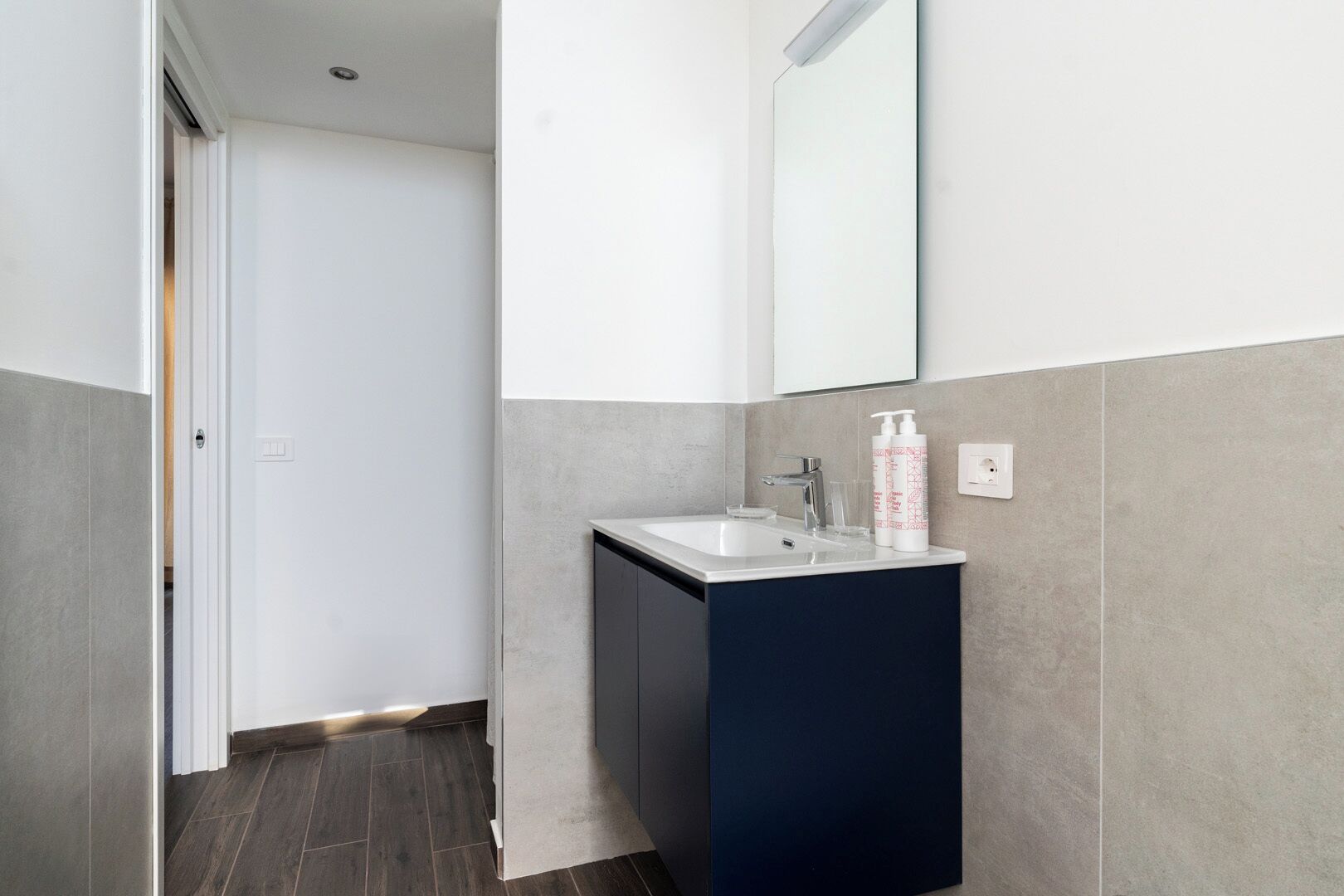 Un baño moderno con un lavamanos blanco, un mueble oscuro y un espejo grande.