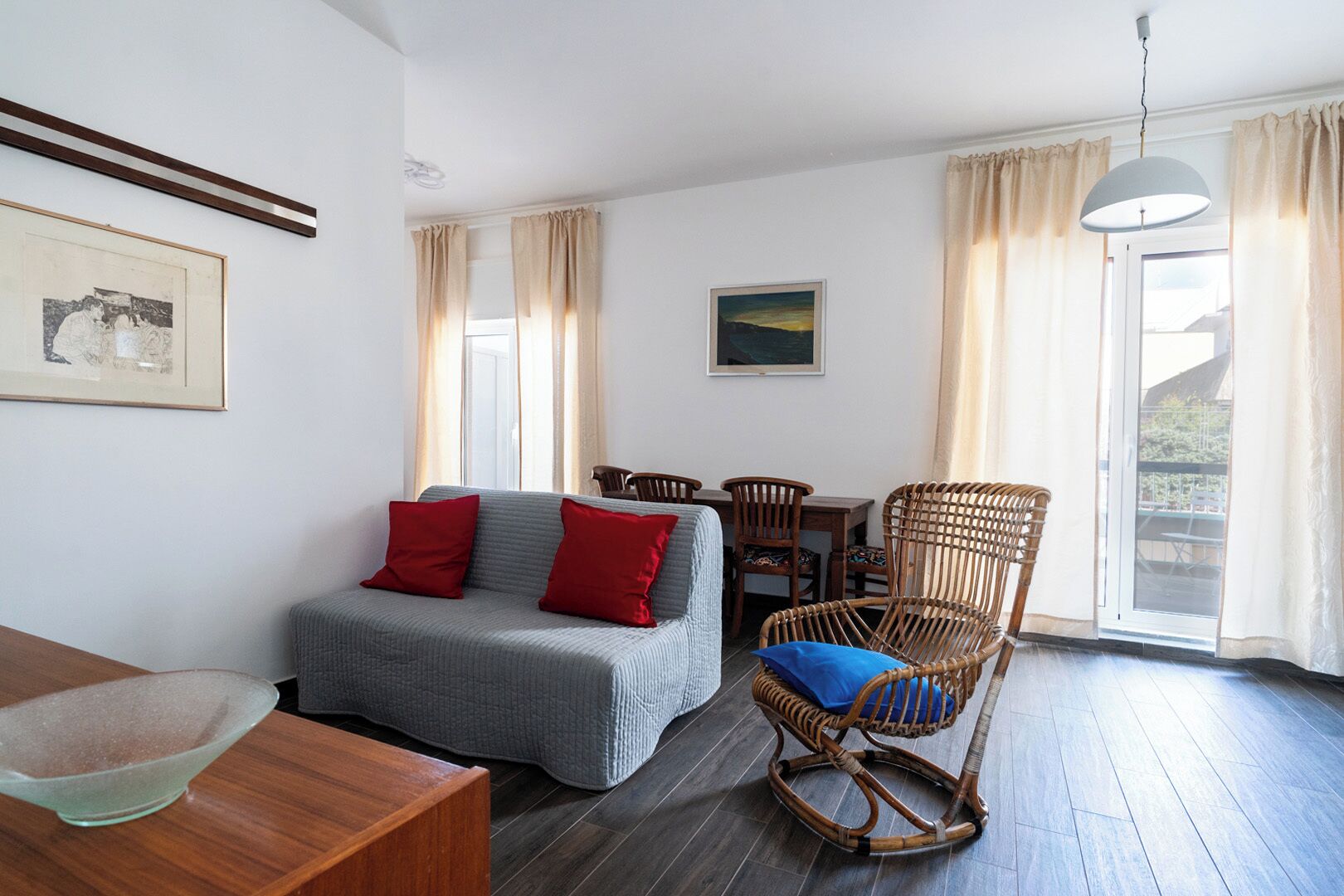 A cozy room with a grey sofa, a wicker chair, a dining table, and a framed picture on the wall.