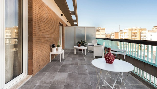 Un balcon doté d’un sol carrelé, de meubles blancs et d’un vase rouge.